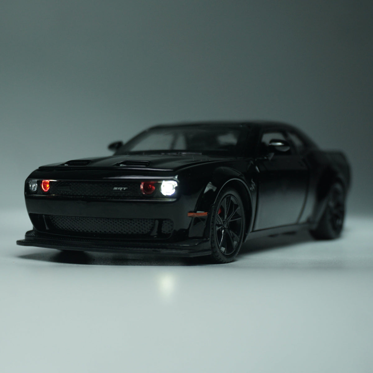 A black die-cast model car resembling a Dodge Challenger SRT, shown from a three-quarter front angle on a neutral gray studio background.
